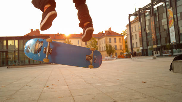 LOW ANGLE: Blue skateboard flipping underneath the young skateboarder's feet.