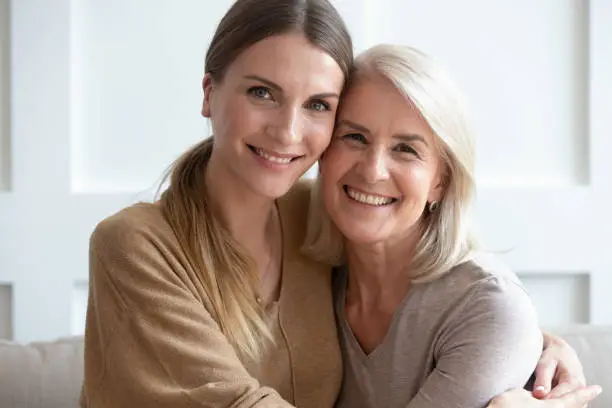 Photo of Attractive aged mother and adult daughter hugging looking at camera