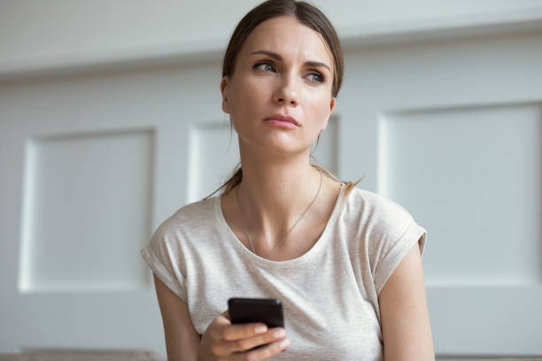 Sad woman holding smartphone waiting call from boyfriend feels jealousy Pensive thoughtful young 30s woman holding smartphone look away lost on sad thoughts waiting first step from man, call or text message or date invitation from boyfriend feels jealousy and concerned envy stock pictures, royalty-free photos & images