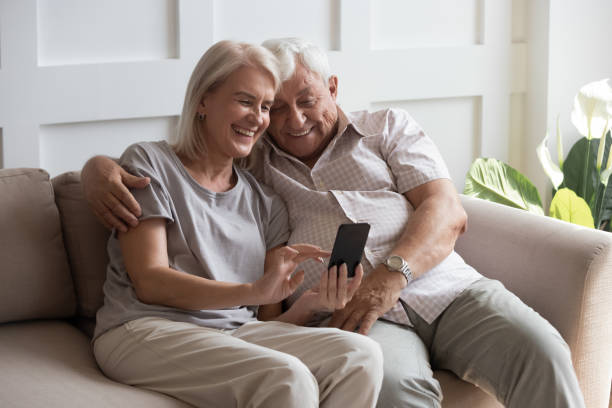 Elderly grandfather and grandmother spend time having fun using smartphone Elderly grandfather and grandmother spend time having fun using smartphone apps, middle-aged wife enjoy online entertainments, taking selfie with old husband, older generation and modern tech concept grandfather photos stock pictures, royalty-free photos & images