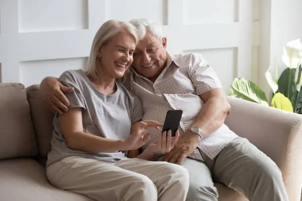 Photo of Elderly grandfather and grandmother spend time having fun using smartphone