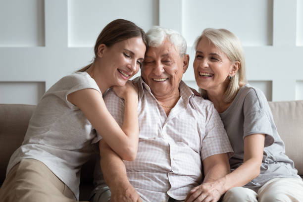 Cheerful three-generation family sitting on couch enjoy time together Happy three-generation family hugging sit on sofa enjoy time together at home, laughing grown up daughter with 70s dad and middle-aged 50s mom warm relations, intergenerational relative people concept father daughter 80s stock pictures, royalty-free photos & images