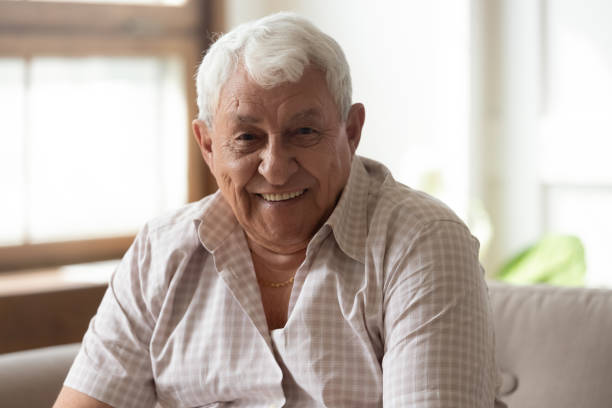 istock Elderly man seated on couch smiles looking at camera 1182248143
