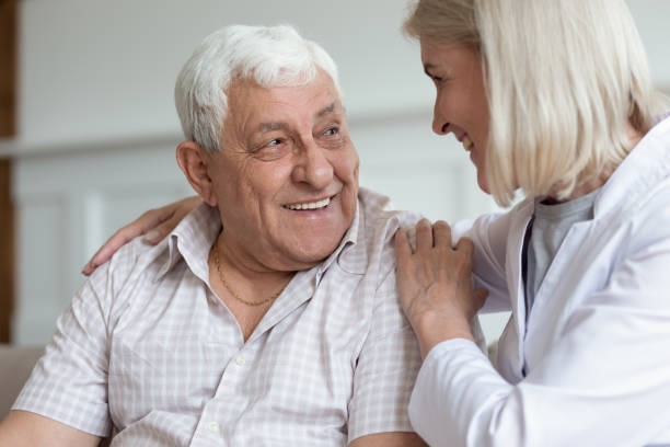 istock Middle-aged nurse hug elderly man patient sitting on couch 1182248163