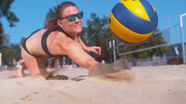 CLOSE UP: Young female volleyball player dives into the sand to save a point. CLOSE UP, DOF: Young female volleyball player dives into the hot sand to save a point during a competitive beach volleyball match. Young Caucasian woman in bikini jumps and hits the ball with one hand beach volleyball stock pictures, royalty-free photos & images