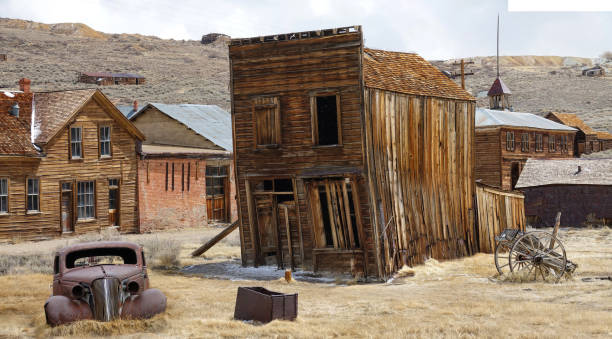 Rusty vintage car and idyllic wooden houses decay in the American wilderness. Rusty vintage car and idyllic wooden houses decay in the American wilderness after the gold rush. Scenic view of a ghost town in the Californian countryside slowly falling apart in rugged conditions. ghost town stock pictures, royalty-free photos & images