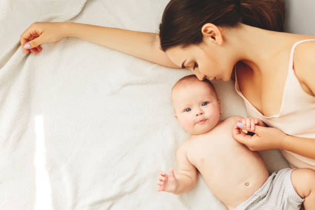 young beautiful mother lies with the baby on the bed, gently kisses, sleeping together Young beautiful mother lies with the baby on the bed, gently kisses, sleeping together. baby sleeping bedding bed stock pictures, royalty-free photos & images