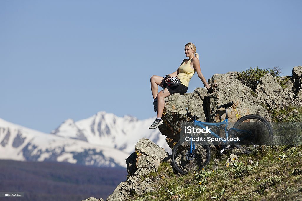 Loira Linda mulher sentada na parte de cima da Rocha em montanhas - Foto de stock de Ciclismo royalty-free