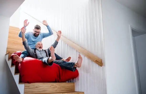 Photo of An adult hipster son and senior father indoors at home, having fun.