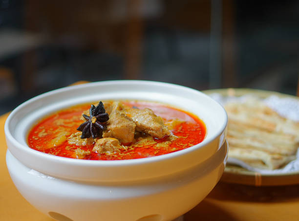 istock Red chicken meat curry with aniseed in ceramic bowl and fried flat bread in round bamboo plate on yellow wood table 1182269348