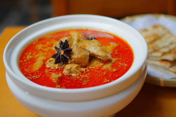istock Red curry with anises in white ceramic bowl and fried flatbread in round bamboo plate on yellow wooden table 1182269349