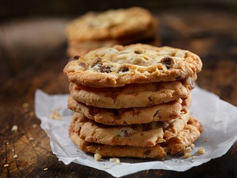 Fresh Chocolate chip cookies stacked on a plate covered in crinkled wax paper. Golden brown, hot out of the oven