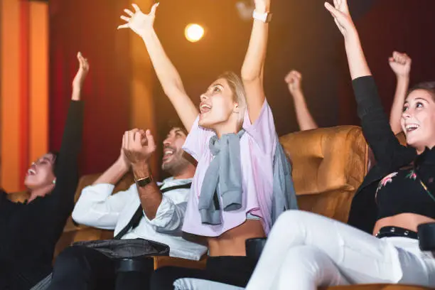 Happy and fun group of people watch cinema and arm up in movie theater