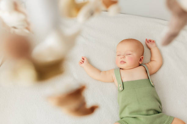 kleines baby mädchen schläft auf einem bett in einem grünen anzug spielmobil dreht sich um sie. - phone cradle stock-fotos und bilder