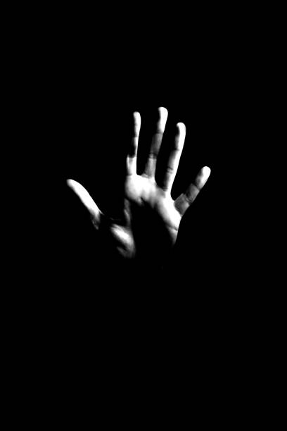 Spooky background. Hand in a dark. Horror background. Violence against women concept. Domestic violence. Human's hand showing gesture stop. Black and white studio shot. silhouette of a stop stock pictures, royalty-free photos & images