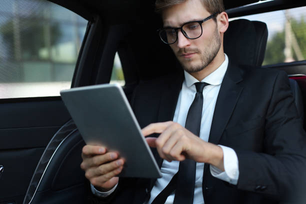 istock Thoughtful young businessman sitting in the luxe car and using his tablet. 1182291435