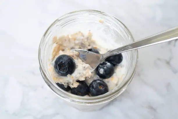 Overnight oats with chia seeds, blueberries and yogurt, on a white marble background.
