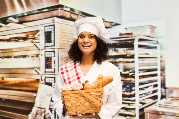 One person / waist up / looking at camera / portrait of beautiful curly hair african ethnicity / african-american ethnicity female / young women / one young woman only baker / photography / retail occupation relaxing / standing at the bakery / desert / restaurant in the store wearing apron who is cheerful / happy / smiling who is baking / pointing and holding cupcake / bread / bun - bread / cake / food and drink / selling / small business / retail / food una persona / cintura para arriba / mirando a la cámara / retrato de hermoso cabello rizado étnico étnico africano / etnia afroamericana mujer / mujeres jóvenes / una mujer joven sólo panadero / fotografía / ocupación comercial relajante / de pie en