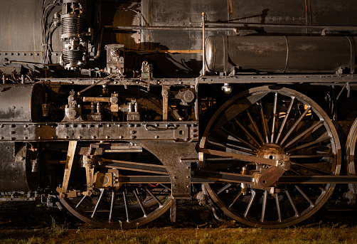 Historic steam locomotive - locomotive wheels and rods close up at night illuminated by lights