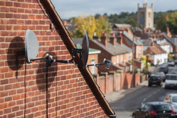 two satellite dishes mounted on a brick house wall with a city background - television aerial roof antenna city imagens e fotografias de stock