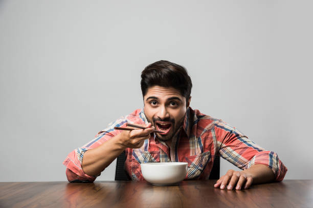 istock empty bowl and Indian man with beard holding spoon or chopsticks, wearing checkered shirt and sitting at table 1182305308