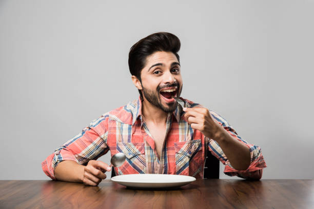 istock empty plate and Indian man with beard holding spoon and fork, wearing checkered shirt and sitting at table 1182306209