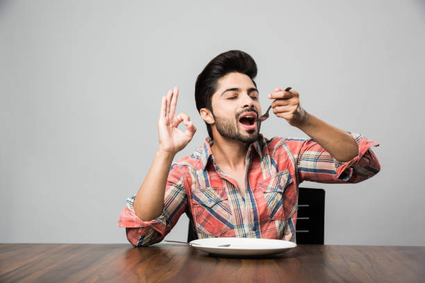 istock empty plate and Indian man with beard holding spoon and fork, wearing checkered shirt and sitting at table 1182306589