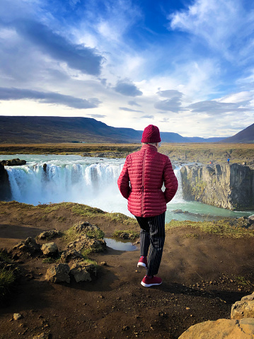 Godafoss, Iceland: A senior woman walking dangerously close to the edge of Godafoss—Waterfall of the Gods—in North Iceland.