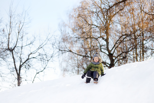 Little boy enjoy riding on ice slide in winter. Outdoor winter activities for family with kids.