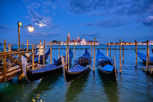 Romantic vacation Venice travel background - gondolas at Saint Mark (San Marco) square and Basilica San Giorgio Maggiore Church seen across Venice lagoon with full moon. Venice, Italy