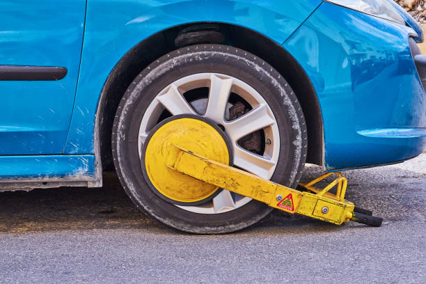 Parked car with an immobilizer tire lock of illegally Clamped front wheel of illegally parked car, yellow clamp attached to wheel car boot stock pictures, royalty-free photos & images