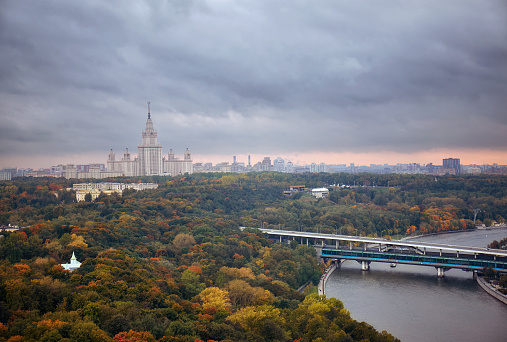 Rainy sunset clouds above river, park, bridge, ships and large city landscape of autumn Moscow