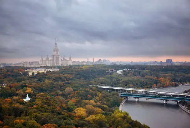Photo of Panoramic aerial view of rainy sunset clouds above river, park, bridge, ships and large city landscape of autumn Moscow