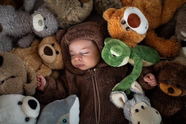 Directly above of baby boy in bear costume sleeping hidden in stuck of stuffed toys on bed