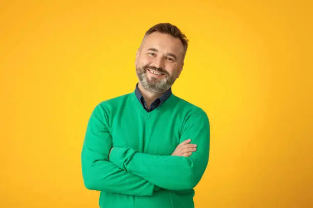 Studio portrait of a 50 year old bearded man in a green sweater on a yellow background