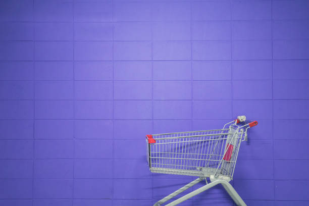 An empty shopping cart against a purple blank wall stock photo