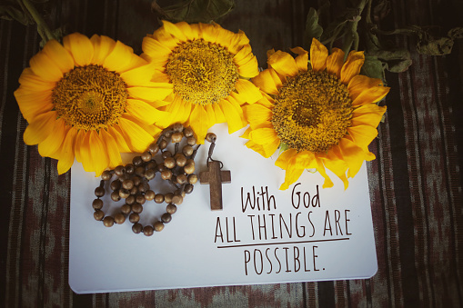 Christianity inspirational quote - With God all things are possible. With wooden Rosary, sunflowers, notebook white paper arrangement background. Words of wisdom concept with Catholic symbol.