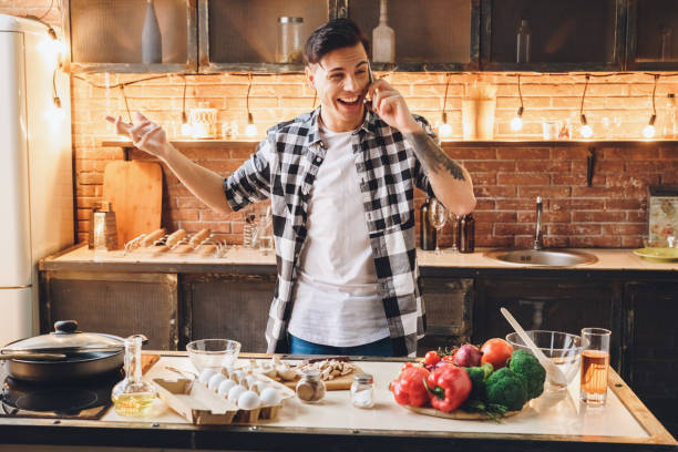 istock Attractive man standing at kitchen, holding phone, toothy smiling 1182341525