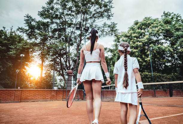 das war ein tolles spiel! abgeschnittene rückansicht von zwei sportlichen athletinnen auf dem tennisplatz. mädchen und ihr tennislehrer gehen auf den tennisplatz. familienfreizeit. - the great court stock-fotos und bilder