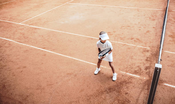 屋外クレーコートでテニスをしている子供。オープンテニスコートの小さなテニス選手のトップビュー。クラブでのテニストレーニングでスポーティな女の子のフルレングスショット。子供� - tennis court sports training tennis net ストックフォトと画像