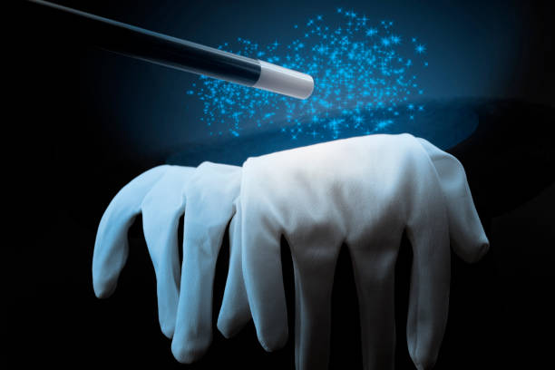 istock Magic show props, live entertainment and artistic performance conceptual idea with black top hat, white magician gloves and wand or baton creating blue pixie dust magical illusion  on dark background 1182343931