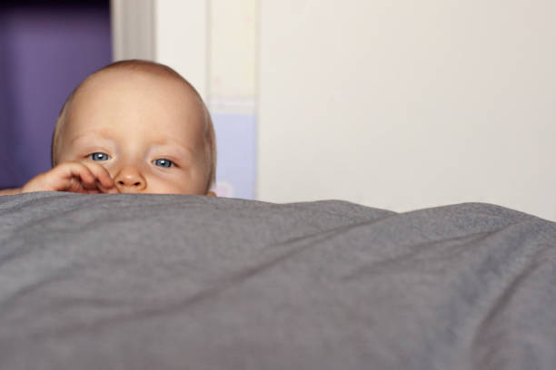 istock Curiosity. A curious baby's face peeks out over the bed. Education, interest, emotions. Face close up. 1182351472