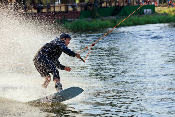 wakeboarder pędzi przez wodę z dużą prędkością wzdłuż trawiastych brzegów rzeki. - wakeboarding waterskiing water sport stunt zdjęcia i obrazy z banku zdjęć