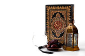 Muslim religious tradition, holy month of Ramadan, Islam and Iftar concept theme with a bowl of dates, prayer beads, glass of water, Quran and arabic lantern on white background with copy space