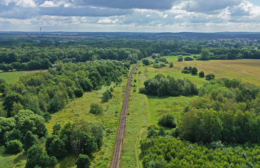 Aerial drone perspective view on straight curved railroad in rural scenery with green forest during summer.