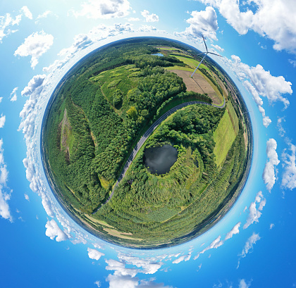 Aerial drone 360 degree view on wind turbine, snake shape road, wheat fields and forest during summer.