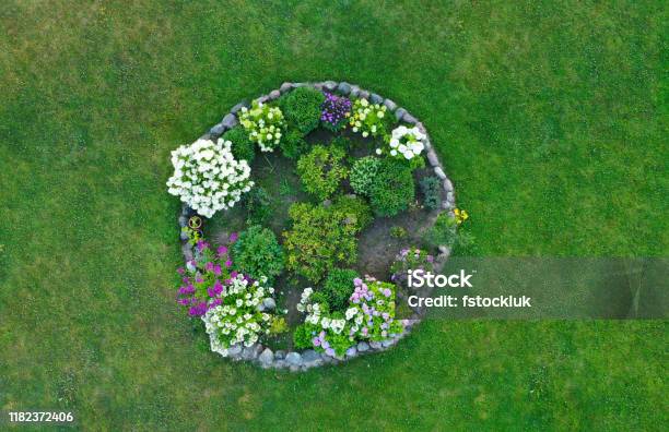 Aerial Drone Top Down View On Stylish Round Flowerbed Surrounded By Rock Wall With Violet White And Yellow Blooming Flowers Grass As Background Stock Photo - Download Image Now