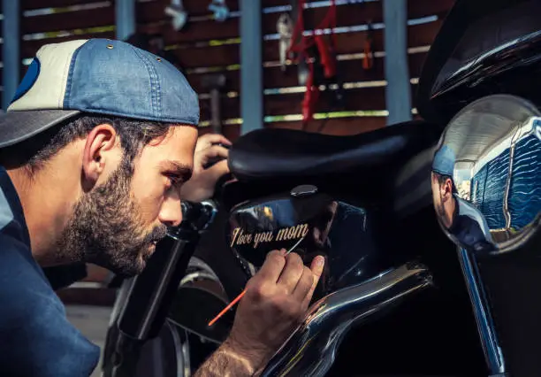 Photo of Signwriter man painting I love you mom in his motorbike