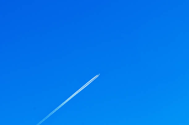 Airplane white smoke contrail tail at high speed cruising in clear empty blue winter sky