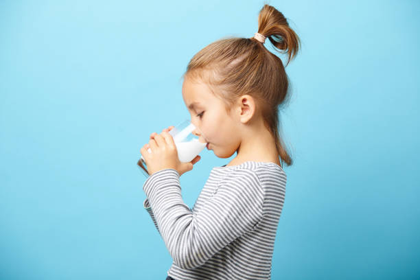 la fille d'enfant boit le lait sans lactose, verticale latérale contre le bleu isolé. - milk child drinking little girls photos et images de collection